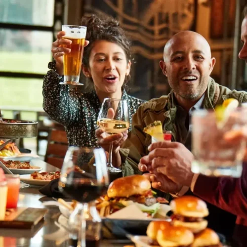 A group of friends enjoying drinks, burgers, and laughter at a restaurant during happy hour, illustrating how to be happy through meaningful social connections and shared moments.