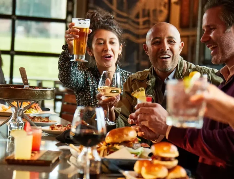 A group of friends enjoying drinks, burgers, and laughter at a restaurant during happy hour, illustrating how to be happy through meaningful social connections and shared moments.