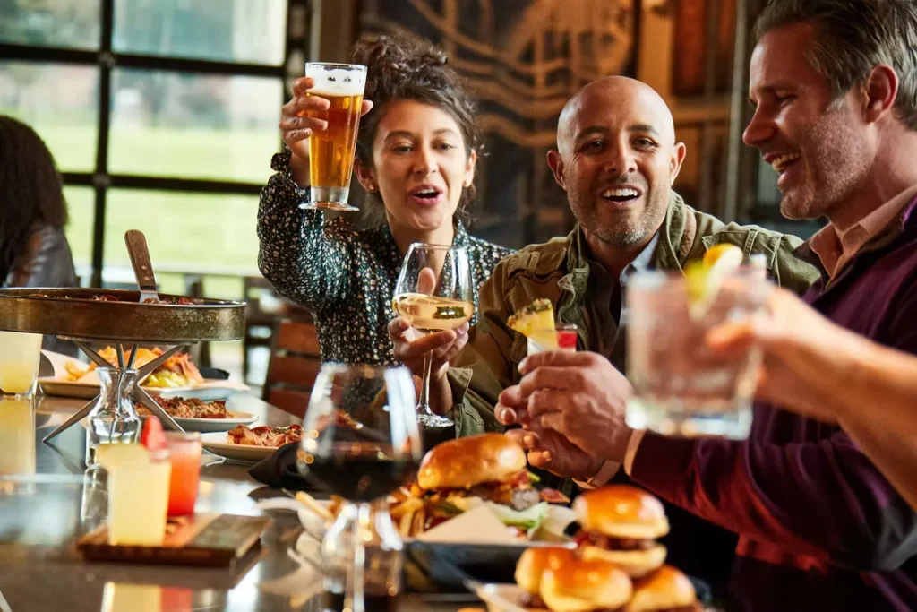 A group of friends enjoying drinks, burgers, and laughter at a restaurant during happy hour, illustrating how to be happy through meaningful social connections and shared moments.