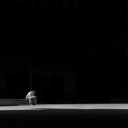 A man sits alone in a dark room, with a faint light illuminating him, symbolizing the quiet solitude and introspection that often accompanies the feeling of loneliness.