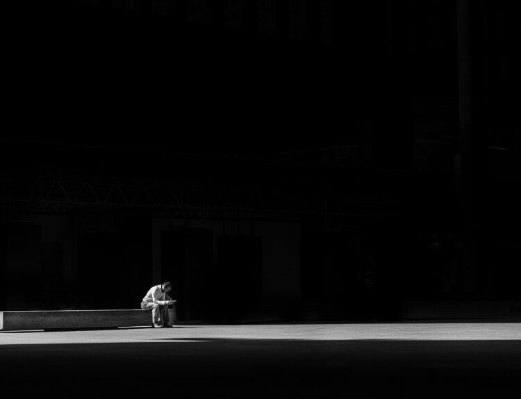 A man sits alone in a dark room, with a faint light illuminating him, symbolizing the quiet solitude and introspection that often accompanies the feeling of loneliness.