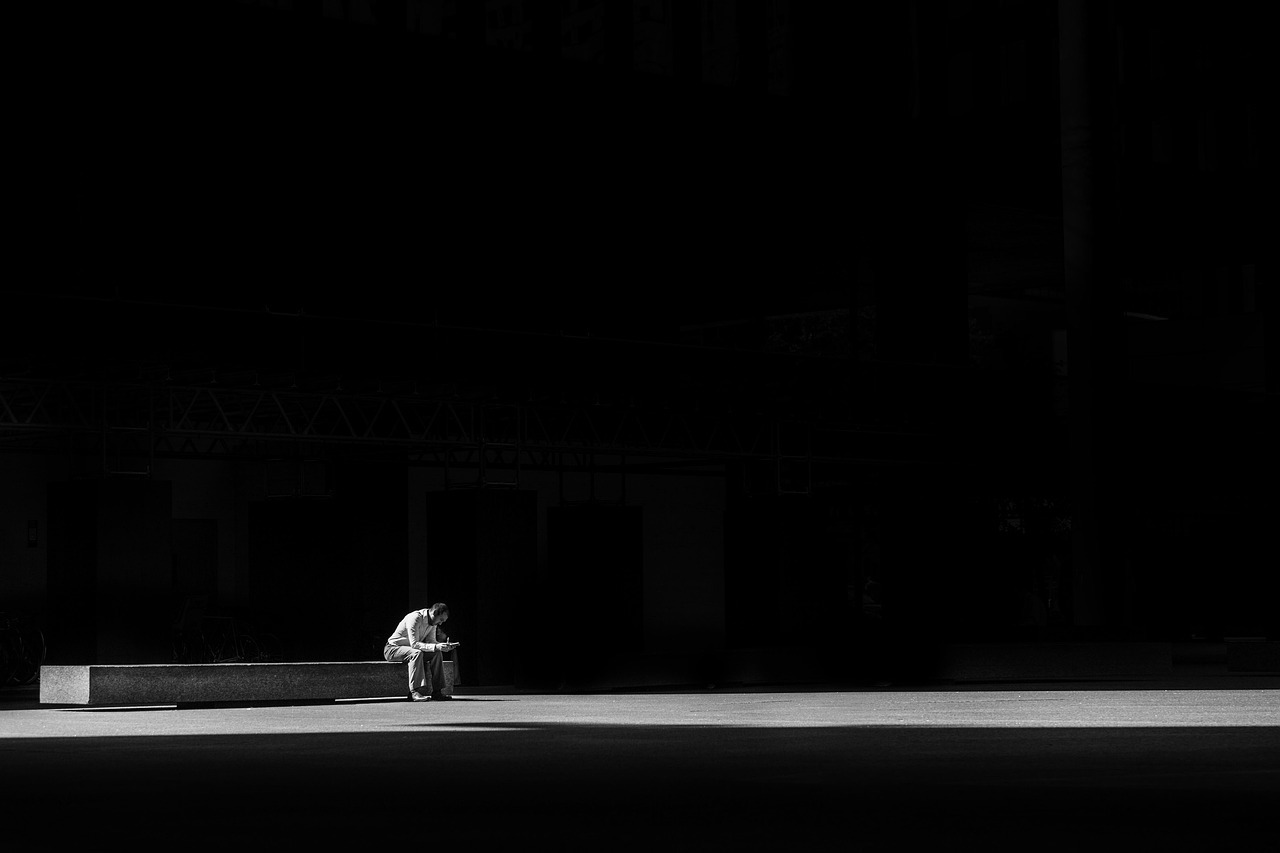 A man sits alone in a dark room, with a faint light illuminating him, symbolizing the quiet solitude and introspection that often accompanies the feeling of loneliness.