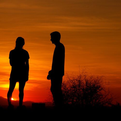 Silhouette of a couple standing apart during sunset, symbolizing emotional distance and trust issues in a relationship.