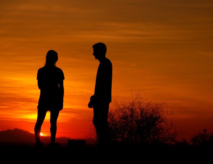 Silhouette of a couple standing apart during sunset, symbolizing emotional distance and trust issues in a relationship.