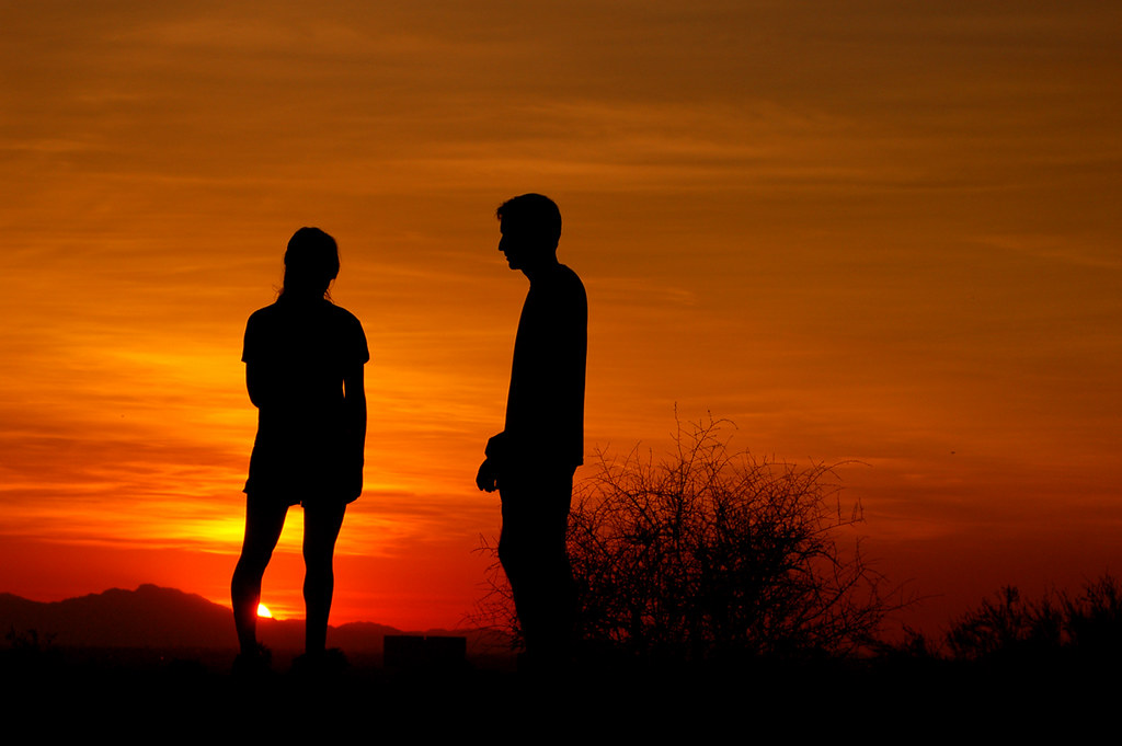 Silhouette of a couple standing apart during sunset, symbolizing emotional distance and trust issues in a relationship.