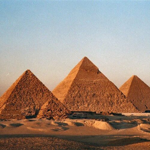 Ancient architectural wonders in the Egyptian desert are displayed by the three Great Pyramids of Giza with a breathtaking sun reflection.