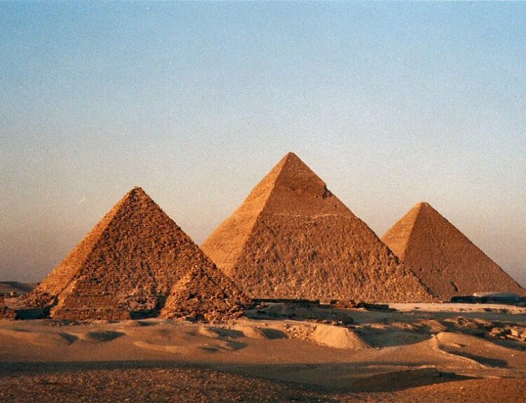 Ancient architectural wonders in the Egyptian desert are displayed by the three Great Pyramids of Giza with a breathtaking sun reflection.