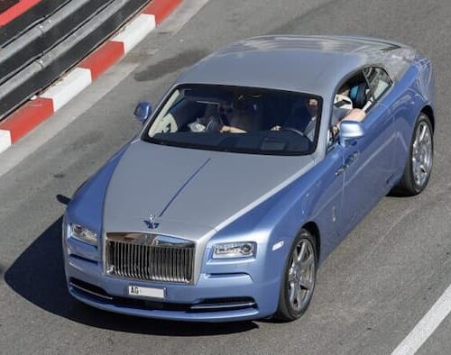 A high-end Rolls-Royce coupe driving on a scenic urban road, showcasing the elegance and craftsmanship of modern luxury cars.