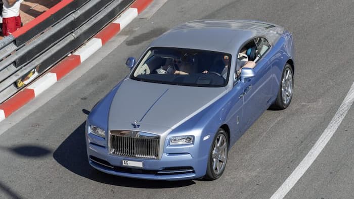 A high-end Rolls-Royce coupe driving on a scenic urban road, showcasing the elegance and craftsmanship of modern luxury cars.