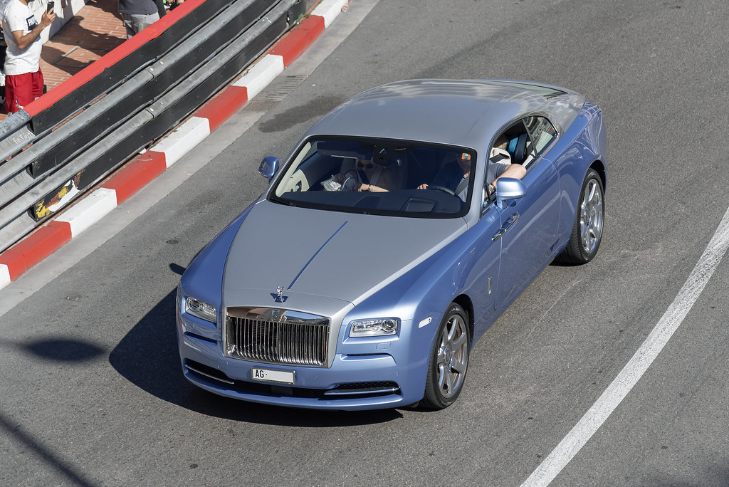 A high-end Rolls-Royce coupe driving on a scenic urban road, showcasing the elegance and craftsmanship of modern luxury cars.
