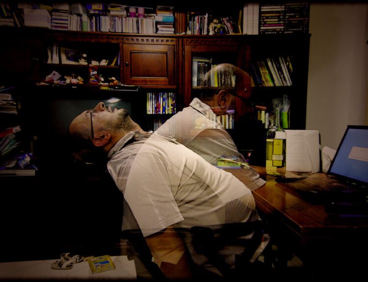 A tired man slumped at a desk with a blurred double exposure effect, symbolizing burnout and overwhelm—highlighting the importance of daily habits to reduce stress and reclaim balance.