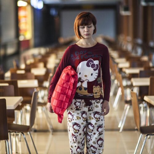 A girl holding a crimson cushion in the center of the cafeteria is sleepwalking in her pajamas.