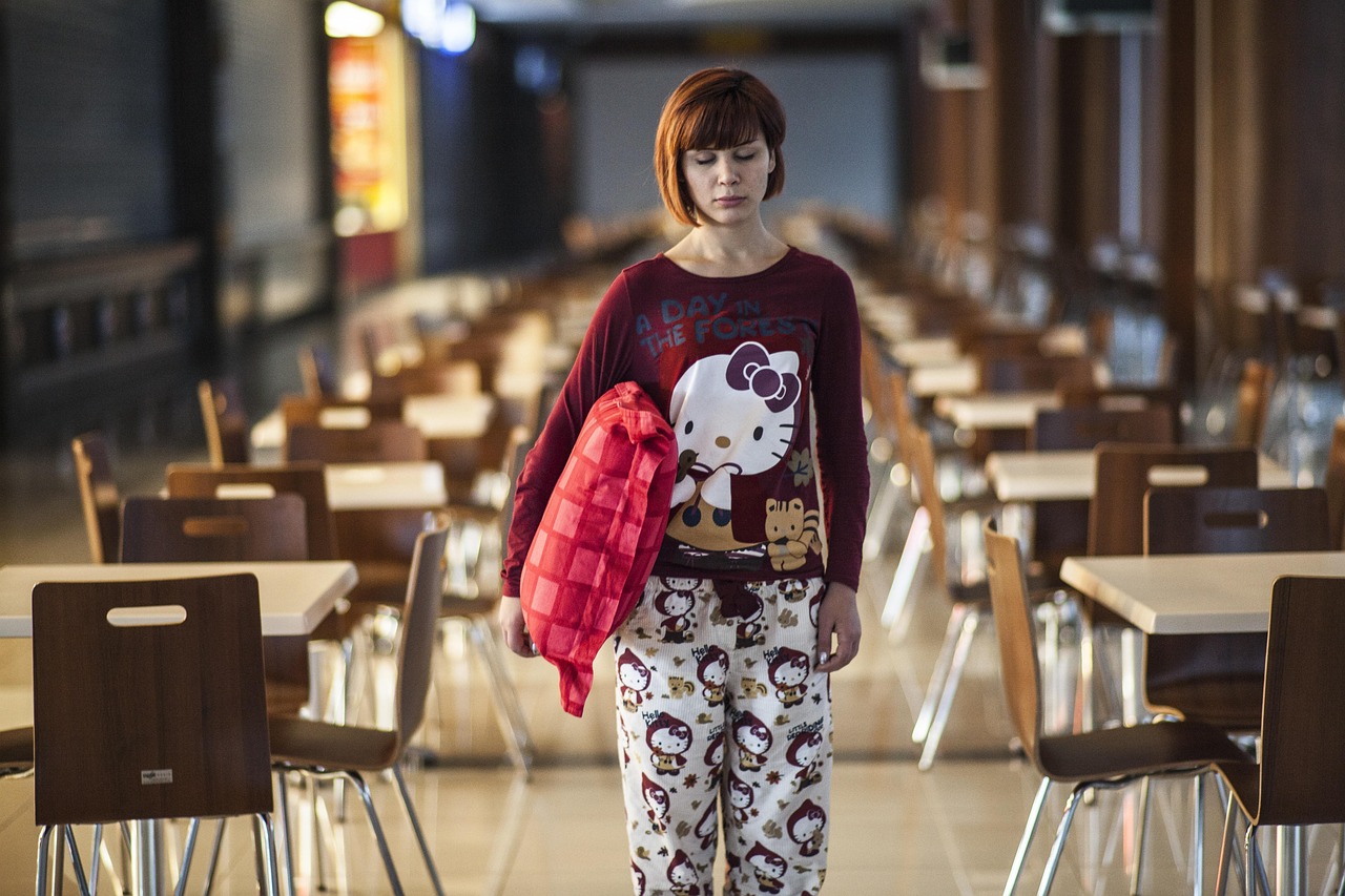 A girl holding a crimson cushion in the center of the cafeteria is sleepwalking in her pajamas.