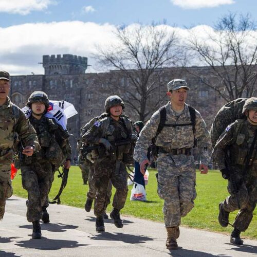 During Korean military service, young Korean soldiers are seen running while wearing heavy equipment, demonstrating their resolve and weariness.