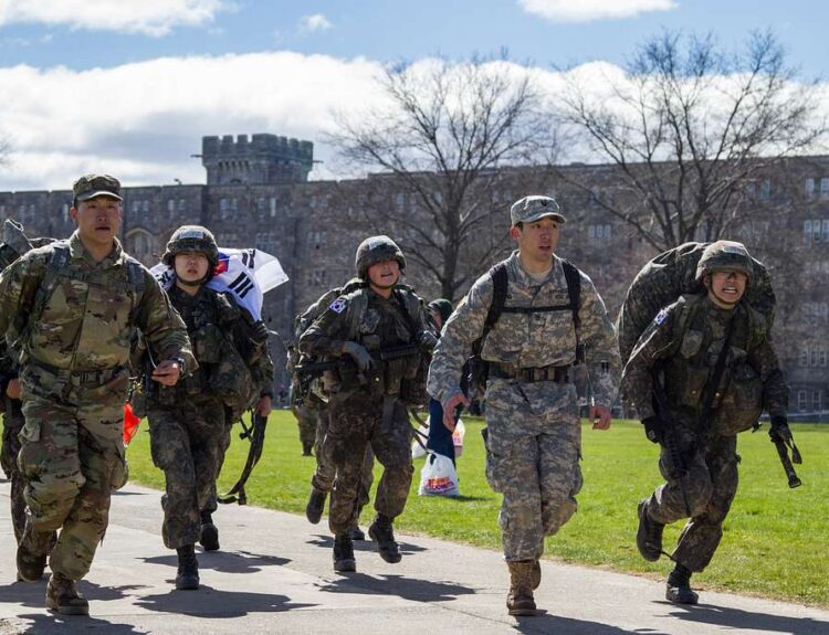 During Korean military service, young Korean soldiers are seen running while wearing heavy equipment, demonstrating their resolve and weariness.